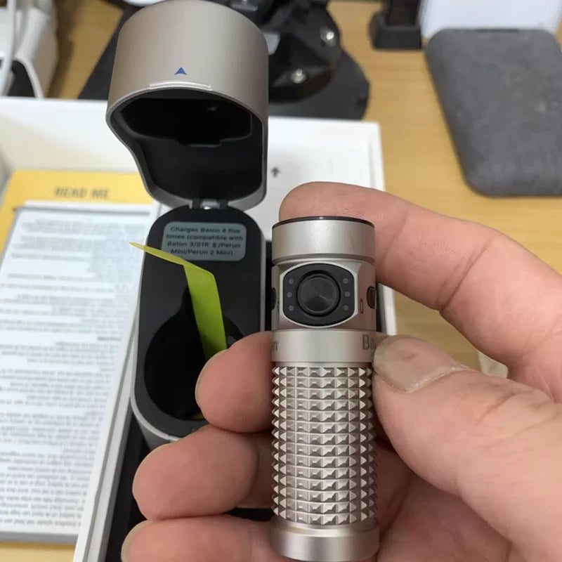 Hand holding a silver electronic device with a textured design, likely a vape pen, against a blurred background.
